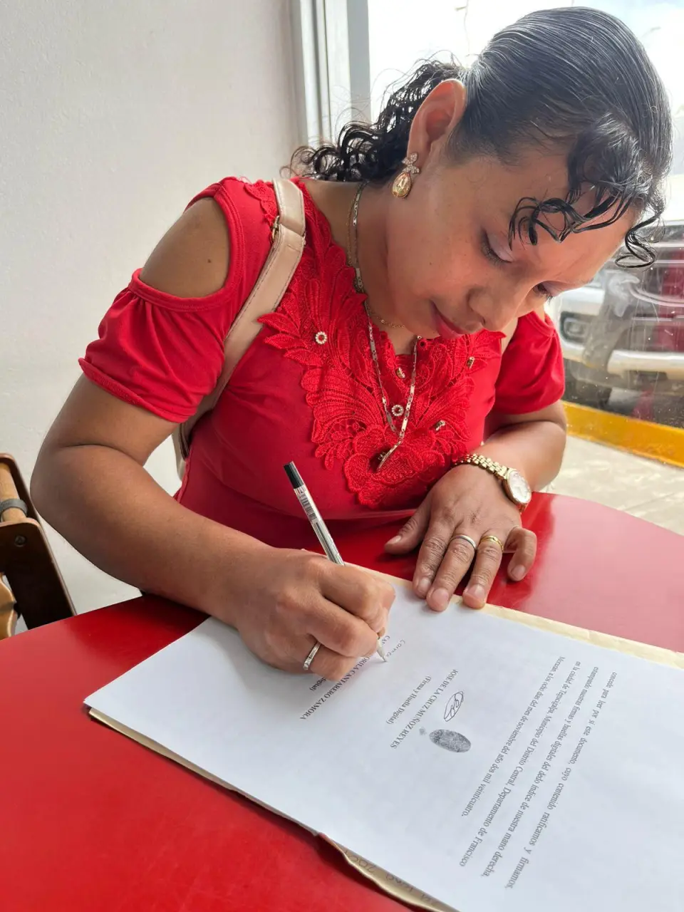 Clienta firma un documento legal sobre una mesa roja durante una gestión presencial de Abogados Catrachos USA.