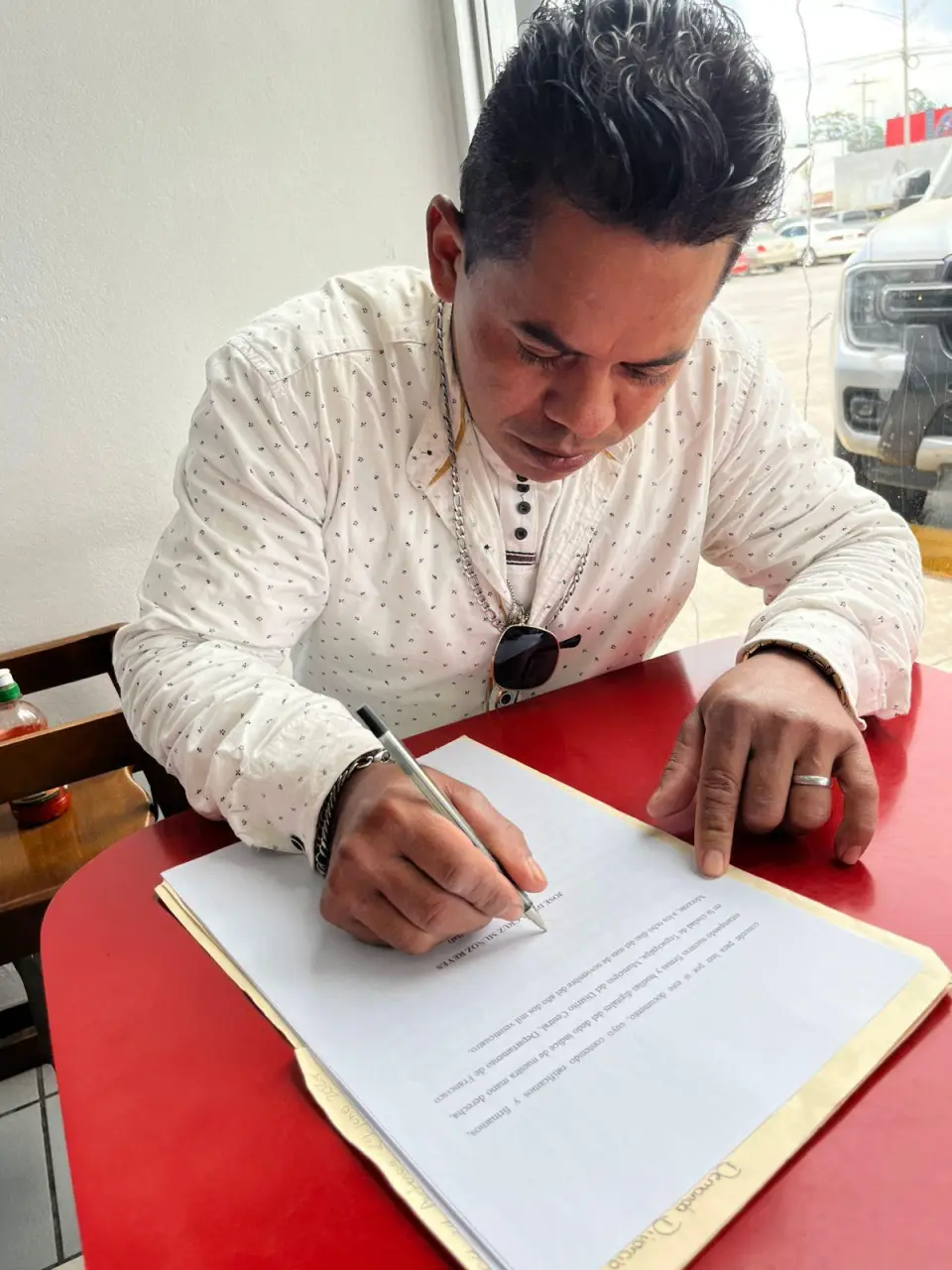 Cliente firma un documento legal sobre una mesa roja durante una gestión acompañada por Abogados Catrachos USA.