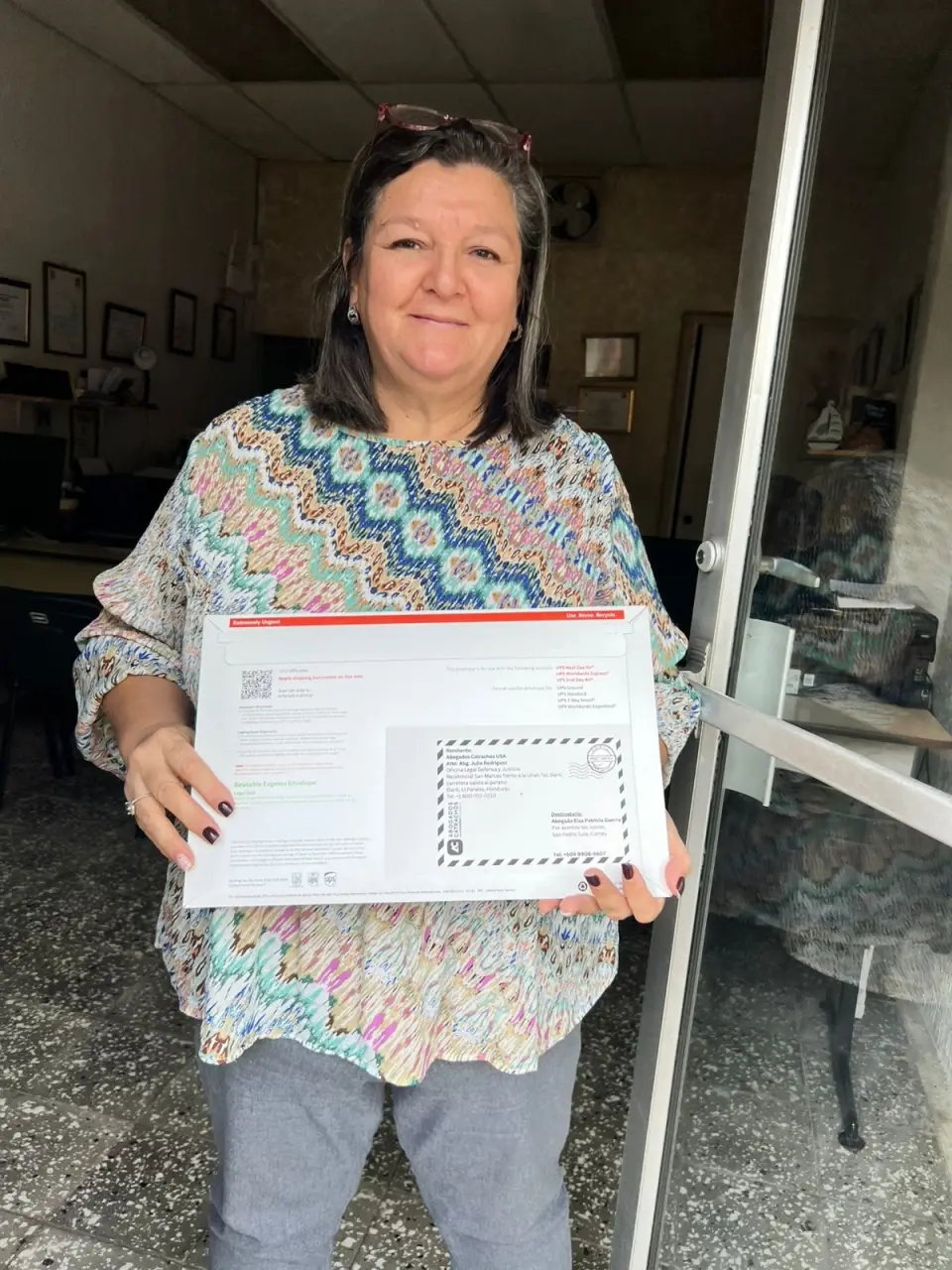 Clienta hondureña sostiene un sobre de documentos legales preparado para envío internacional con el apoyo de Abogados Catrachos USA.