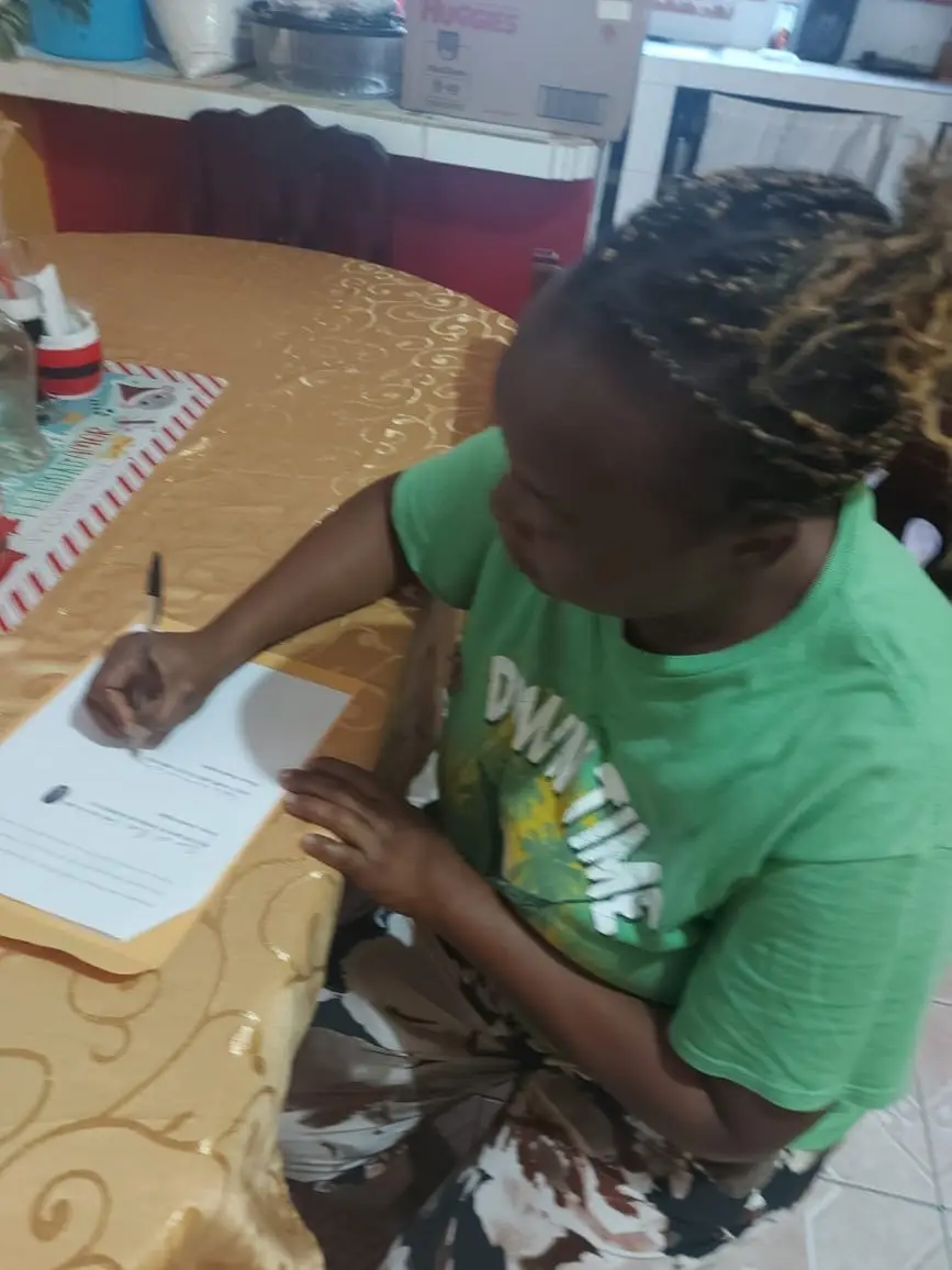 Clienta firma un documento legal en una mesa de comedor durante una gestión acompañada por Abogados Catrachos USA.