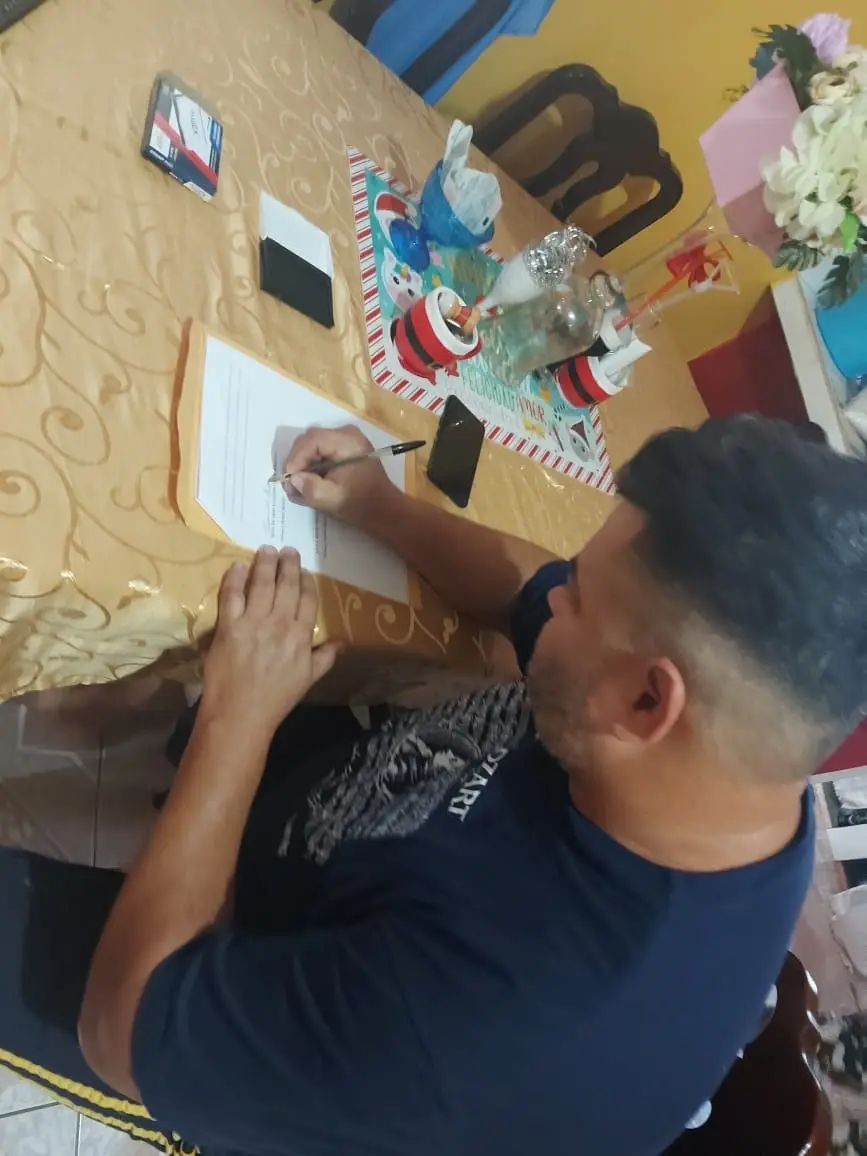 Cliente firma un documento legal en una mesa durante una gestión coordinada por Abogados Catrachos USA.